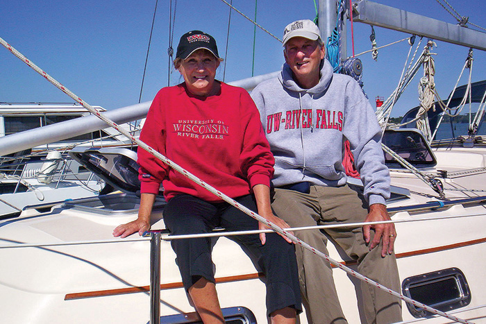 Senior Caucasian male and female sitting on a white boat wearing a red and gray sweatshirts and hats