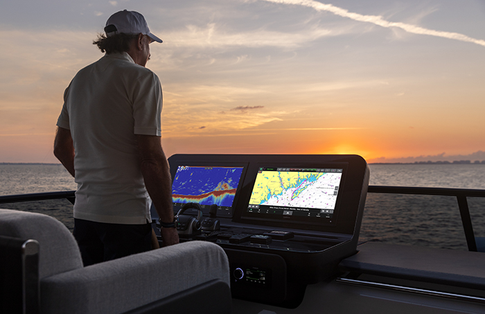 Adult male wearing a white hat and white shirt looking at two radar screens on a boat during sunset.