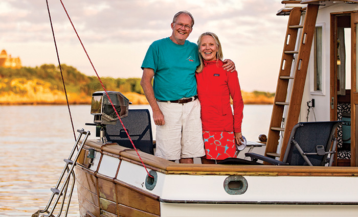 Senior male in blue short-sleeve shirt and senior female in red pullover posing on their boat.