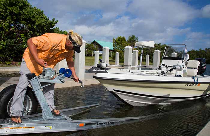 Man bent over looking at incoming boat while on boat trailer at boat launch waiting to attach winch hook to the boat's eye for transporting