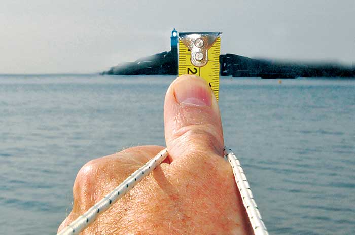 A thumb holding a tape measure pointed at the horizon with a rope tied around it. 