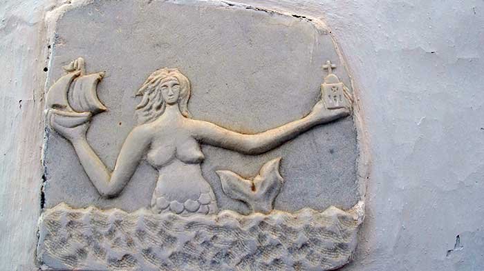 Ancient Greek carving of a mermaid holding a ship and a church in each hand