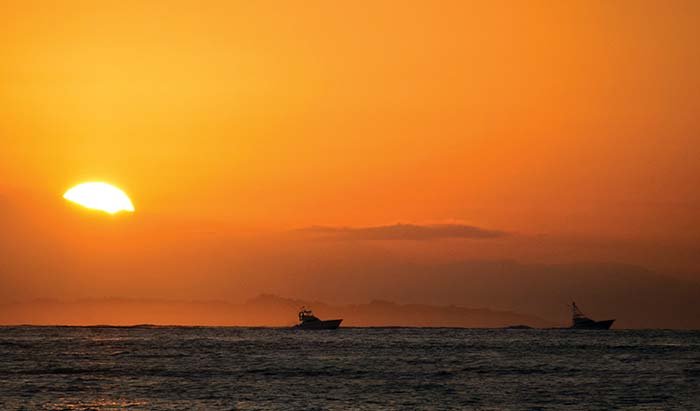 A bright orange sunset with two powerboats outlined in the distance