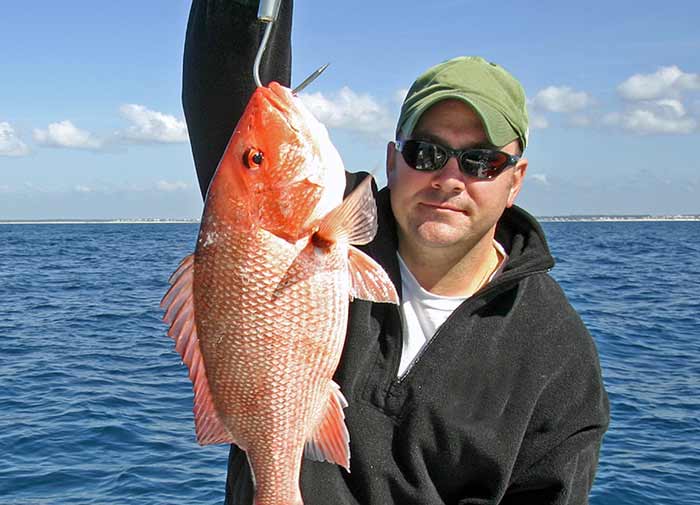 A man holds up a Red snapper catch still on the fishing hook.
