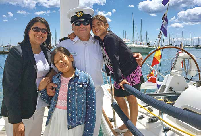 A family of four smile at the camera aboard a sailboat.