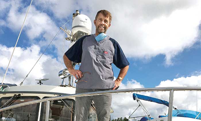 Man with surgical mask around his neck stands on deck of a boat