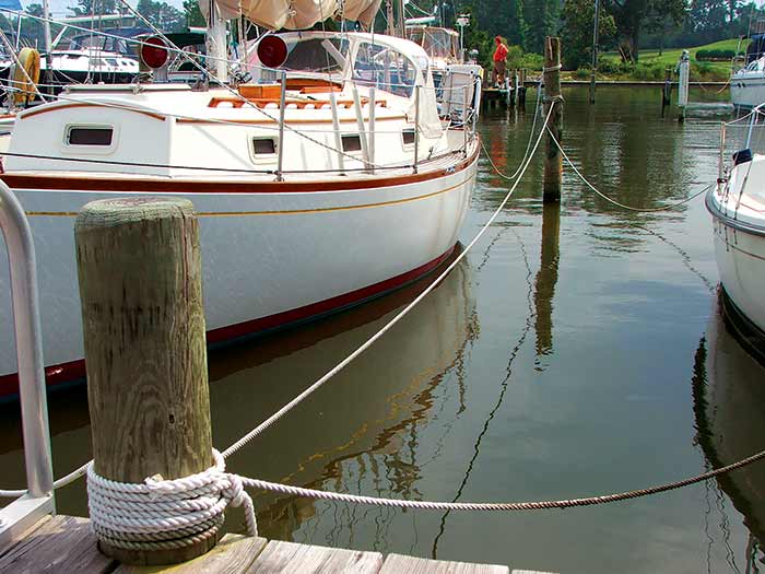 Two sailboats tied up at a marina with their lines tied to the pilings that separate the two slips