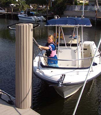 Girl standing  at bow of powerboat using a landing loop to snag a line onto a boat piling