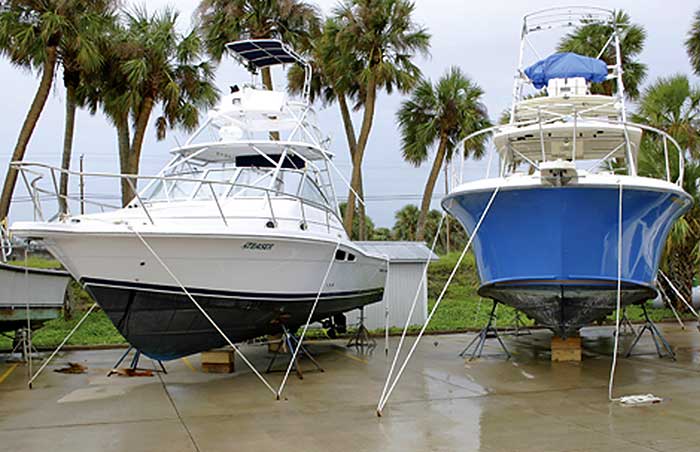 Two powerboats sit on top of metal stands with several ropes extending from the boats into the concrete ground