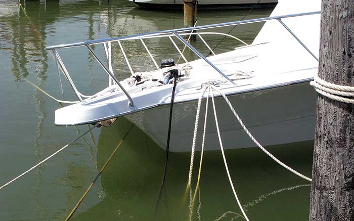 Bow of a sailboat with several lines attached to it and tied around a nearby wooden piling