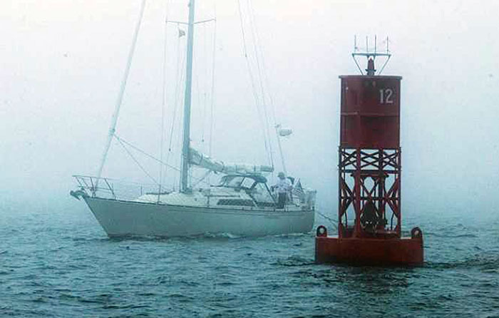 White sailboatwith sails down in thick fog with red buoy right in the foreground