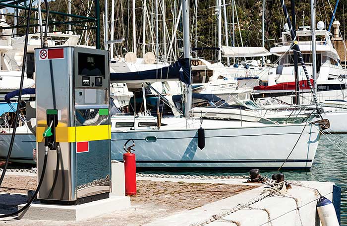 Gas pump at the corner of a dock with a sailboat in the background
