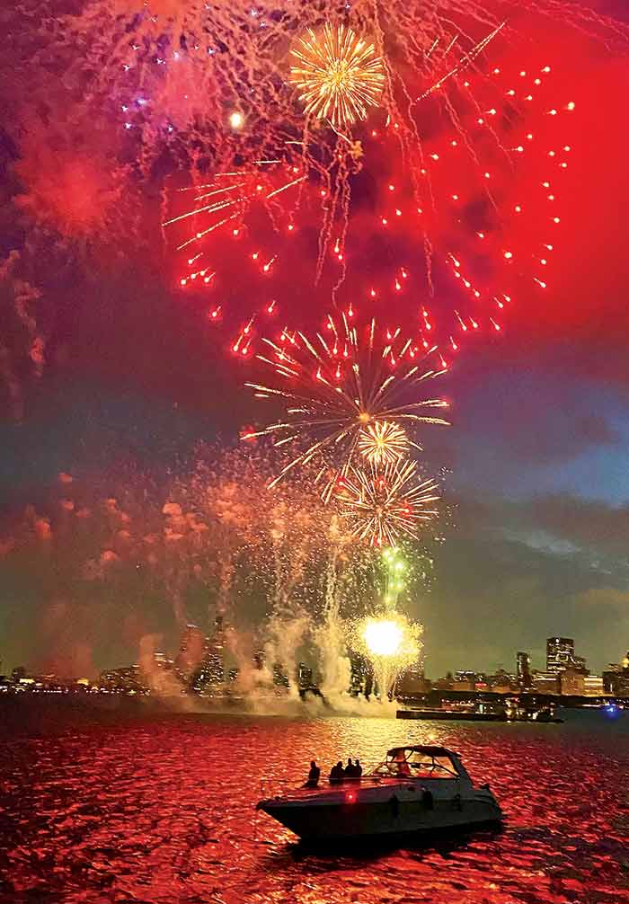Photo Contest Action & Watersports Finalist: Image of red, yellow and purple fireworks erupting over the water with a boat anchored in the forground