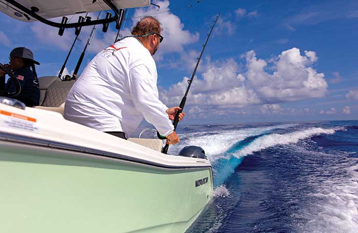 Man wearing a white long-sleeve t-shirt fishing off the bow of a power catamaran as it cruises through the water
