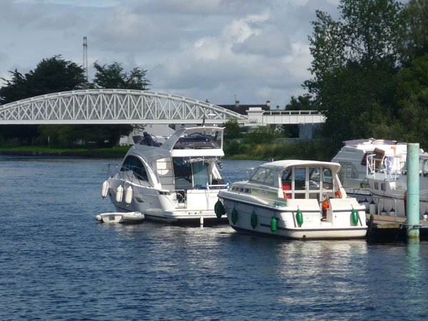 Three boats are navigating a river, with a small metal bridge in front of them