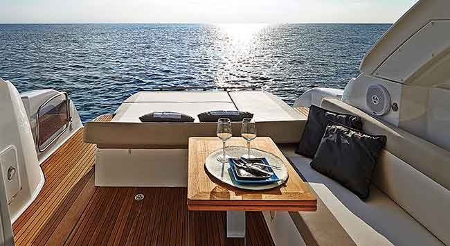 two wine glasses and a place setting in the seating area of a large boat, the sun reflects on the open water 