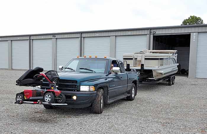 A pickup truck with a scooter attached to the front backs a pontoon boat into a storage garage