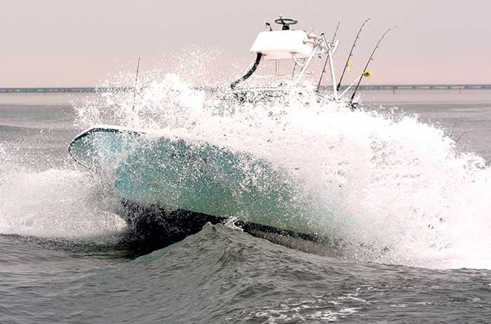 A boat underway gets hit by a large wave on the bow of the boat