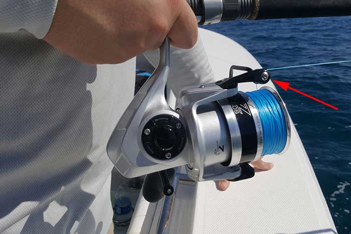 A close up of a fishing reel spinning with blue line attached. 