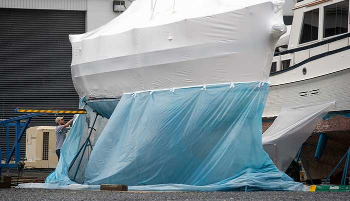 Man applying sheetwrapping to large boat