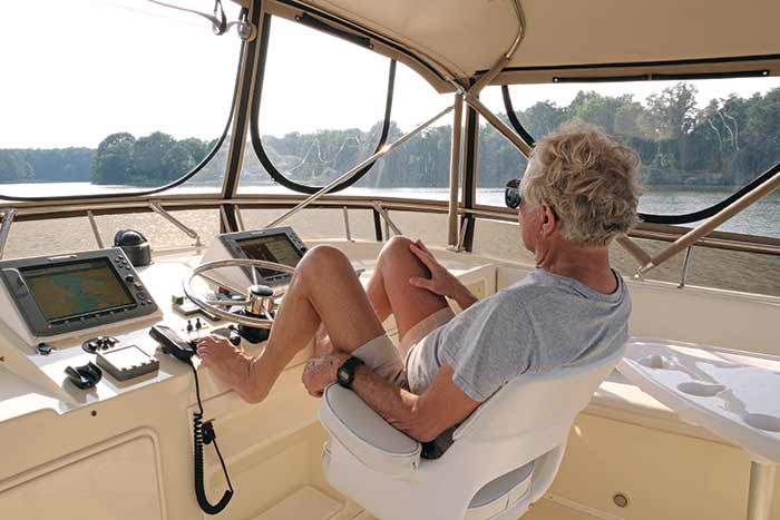 A grey haired man sitting with his feet up at helm of a large powerboat