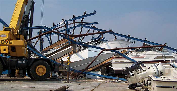 A pile of damaged boats intertwined with a blue structure. A yellow crane in the foreground