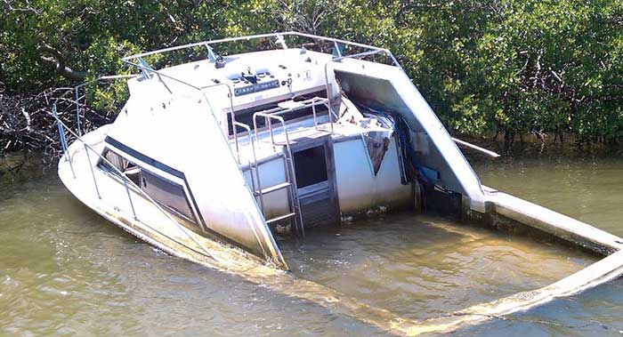 Abandoned white powerboat sinking into swamp water, only the cockpit is visible