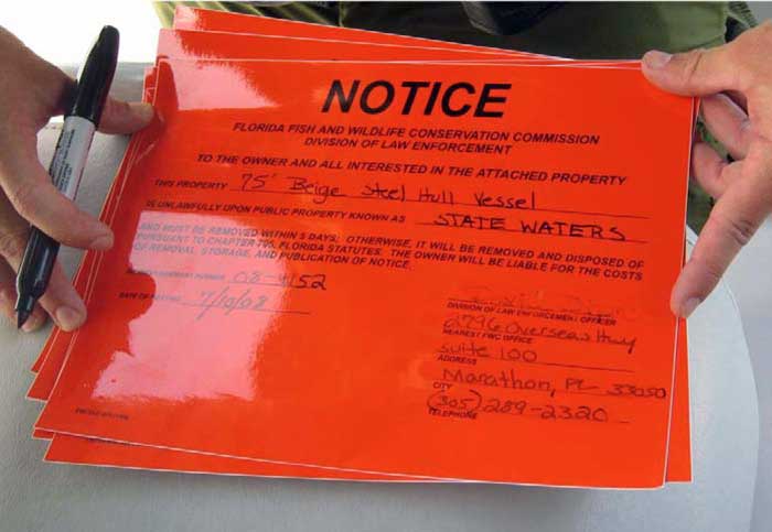 Holding orange Notice Of Removal signs from the Florida Fish and Wildlife Conservation Commission and a black sharpie marker