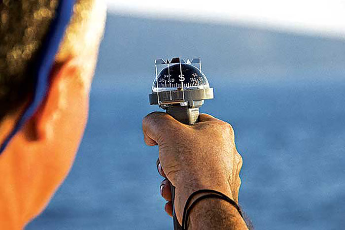 Side-view of a man's face and hand holding up a hand-held compass with blue water in the background