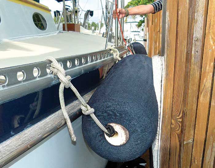 Dark blue colored fender tied and hanging off the side of a boat in the horizontal position between the boat and a dock piling