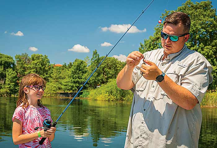Man baiting a fishing hook while young girl stands by watching and holding the fishing rod