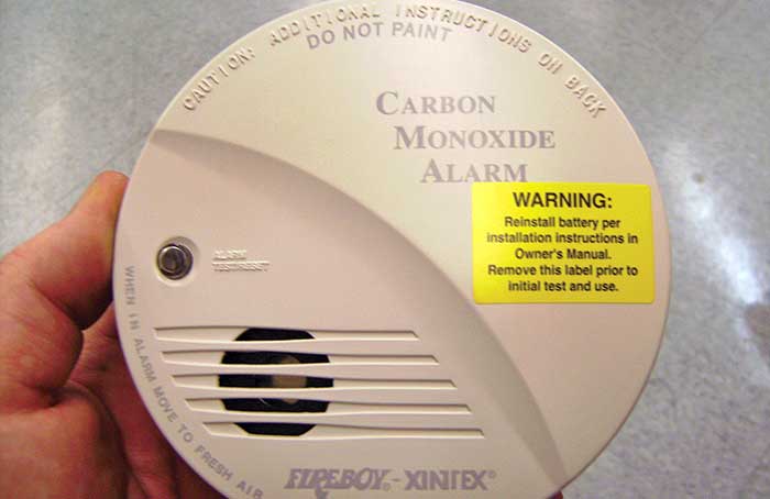 Hand holding carbon monoxide alarm with yellow warning sticker on it