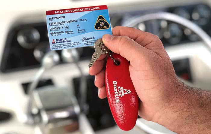 Hand holding a Boater Education Card attached to a BoatUS floating keychain