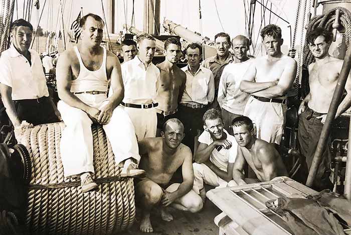 A large group of men aboard a three-masted brigantine ­sailing ship