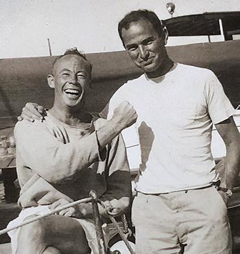 One man sitting and one man standing together aboard a sailboat
