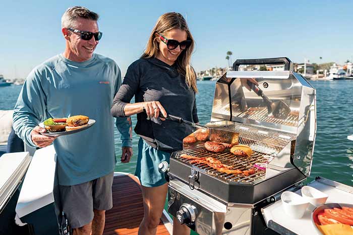 Smiling man and woman griling cheeseburgers and bacon aboard a boat