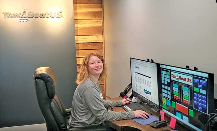 Woman sitting at a desk with two computer screens and a TowBoatUS logo on the wall behind her