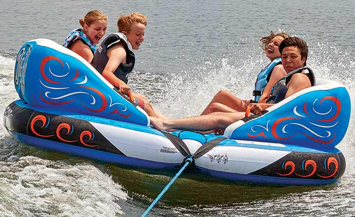 Four children riding on an inflatable tube while being towed through the water