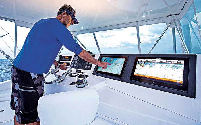 Man standing at boat helm steering the boat while using an electronic chartplotter