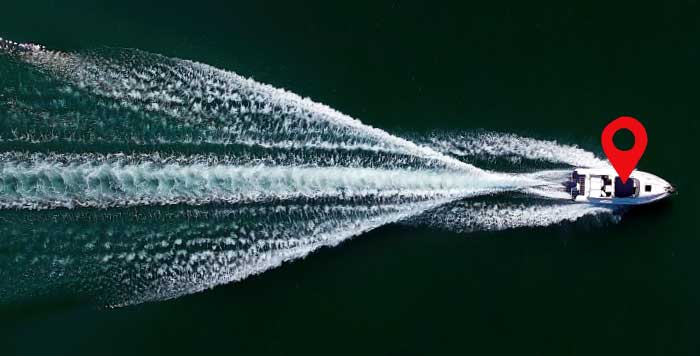 Aerial view of a white powerboat cruising horizontally through the water with a red marker over it