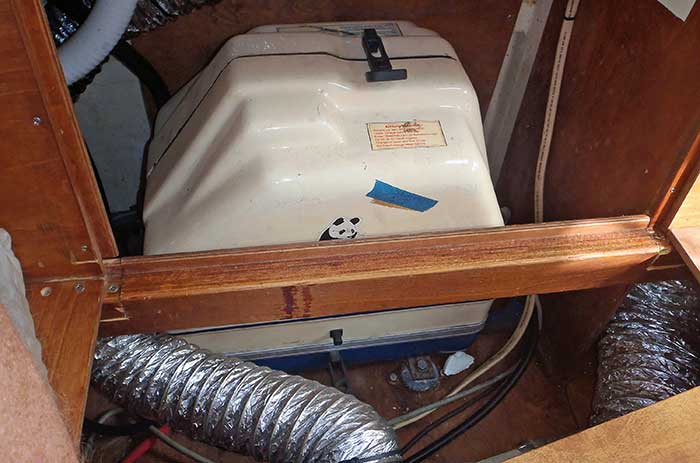 Boat generator installed with a white sound shield with gray hose coming out the left side