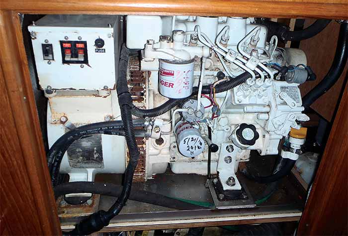 White boat generator with varies wires and hoses attached to it sits in a wooden cabinet