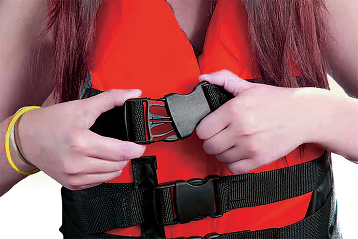 Close-up photo of person clicking the black buckle of a red life jacket around their waist