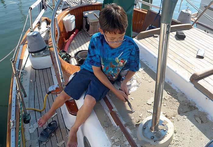 Young boy sitting on the edge of a boat deck removing the nonskid deck surface with a screwdriver