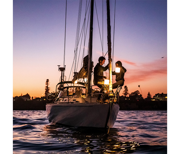Male and female on a white sailboat during sunset hanging lights on the front of the vessel.