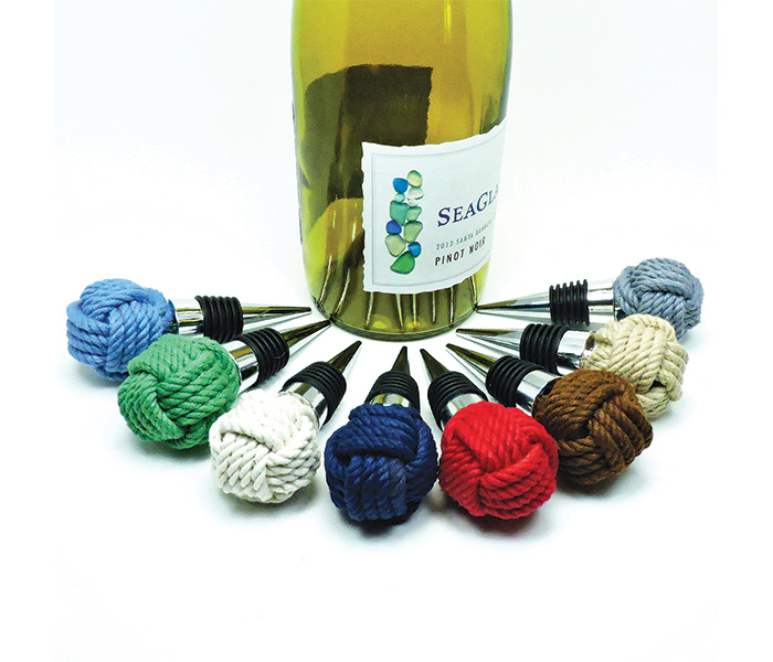 Set of eight multi-color hand made knit wine stoppers surrounding a bottle of wine.
