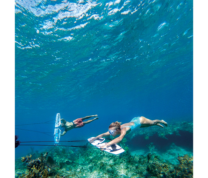 A female diver wearing a blue swimsuit and a male diver wearing red swim trunks underwater exploring.