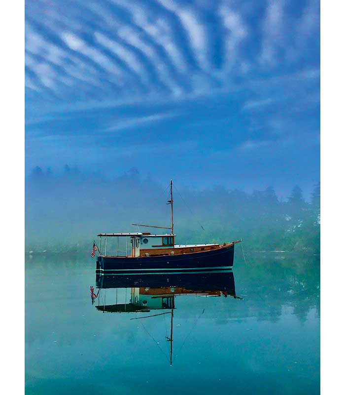 Photo Contest Cover Finalist: Image of a boat at anchor with its reflection on the water and blue sky above