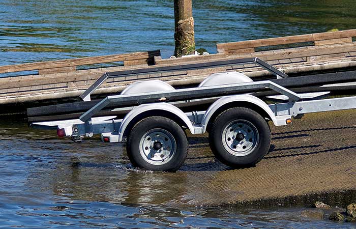 Empty boat trailer sitting at the edge of a boat ramp with its wheels at the waters edge and dock in the background