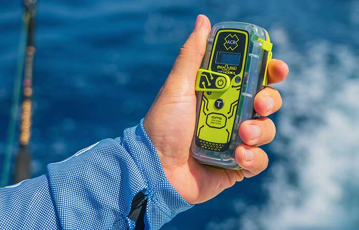 Hand holding a personal locator beacon onboard a moving boat with a fishing rod in the background